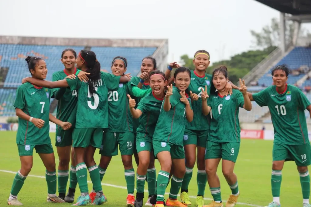 A joyful women's soccer team in Bangladeshi green jerseys, Bangladeshi women's team celebrating on a field. They’re all smiling and making peace signs, conveying excitement and unity. Bangladeshi Women Make History by Qualified for the AFC